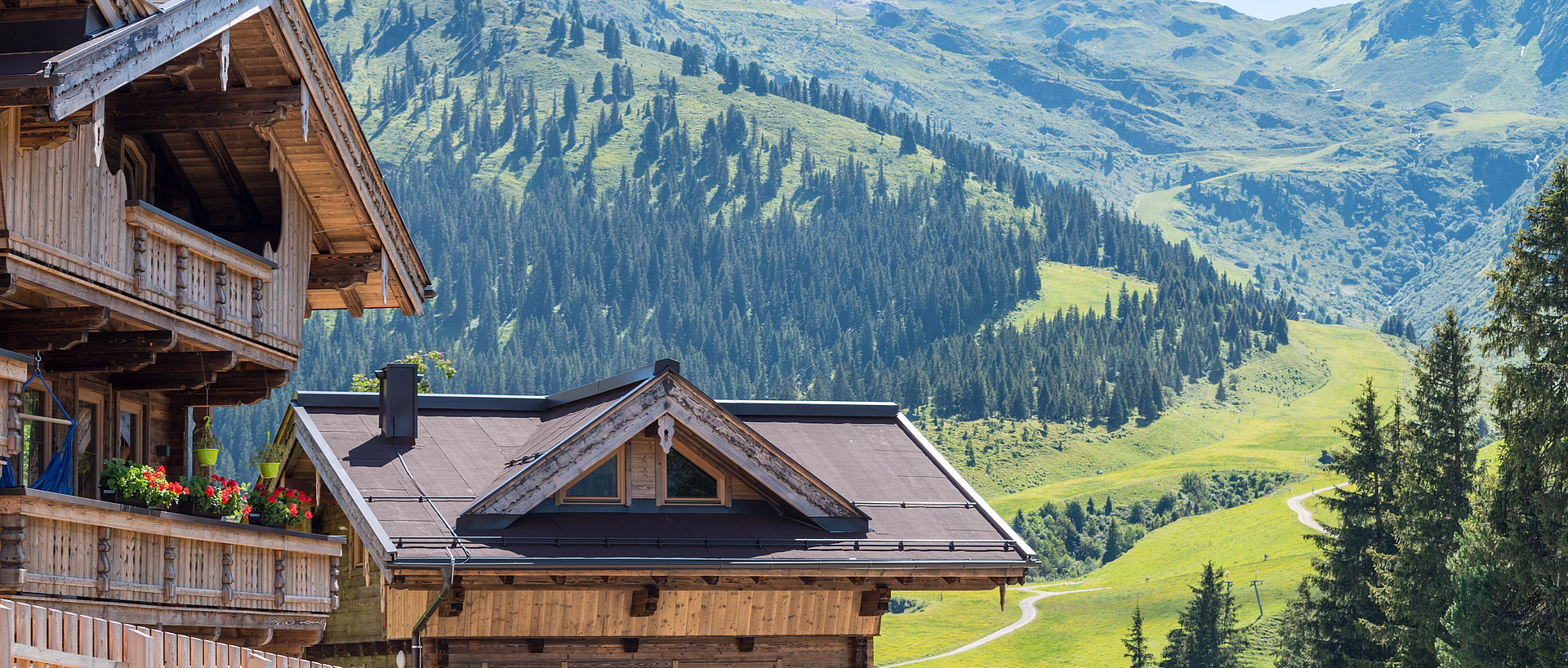 Wooden chalets against an alpine mountain backdrop with green meadows and forests.